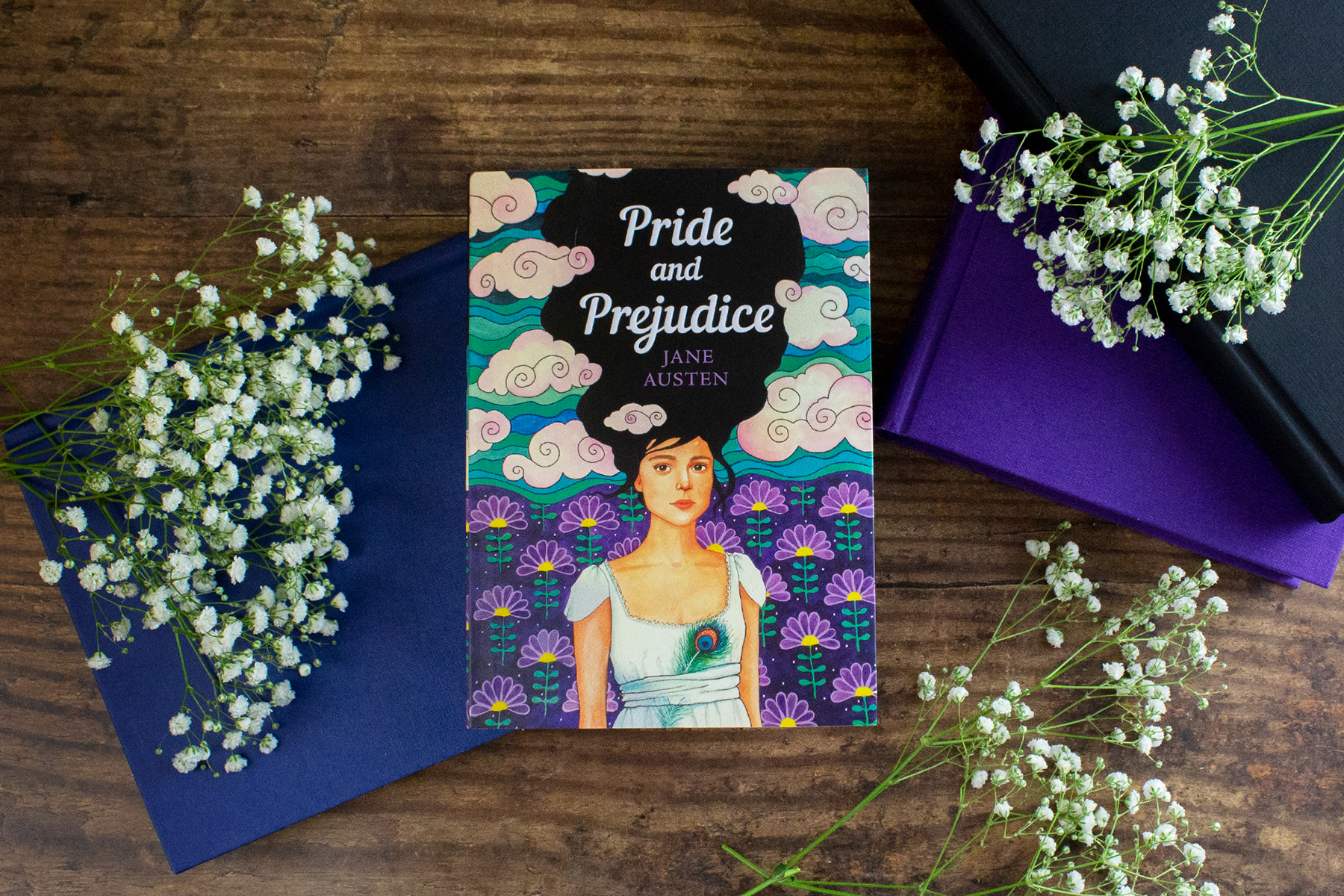 A photo of the book Pride & Prejudice on a wooden table, surrounded by purple books and flowers
