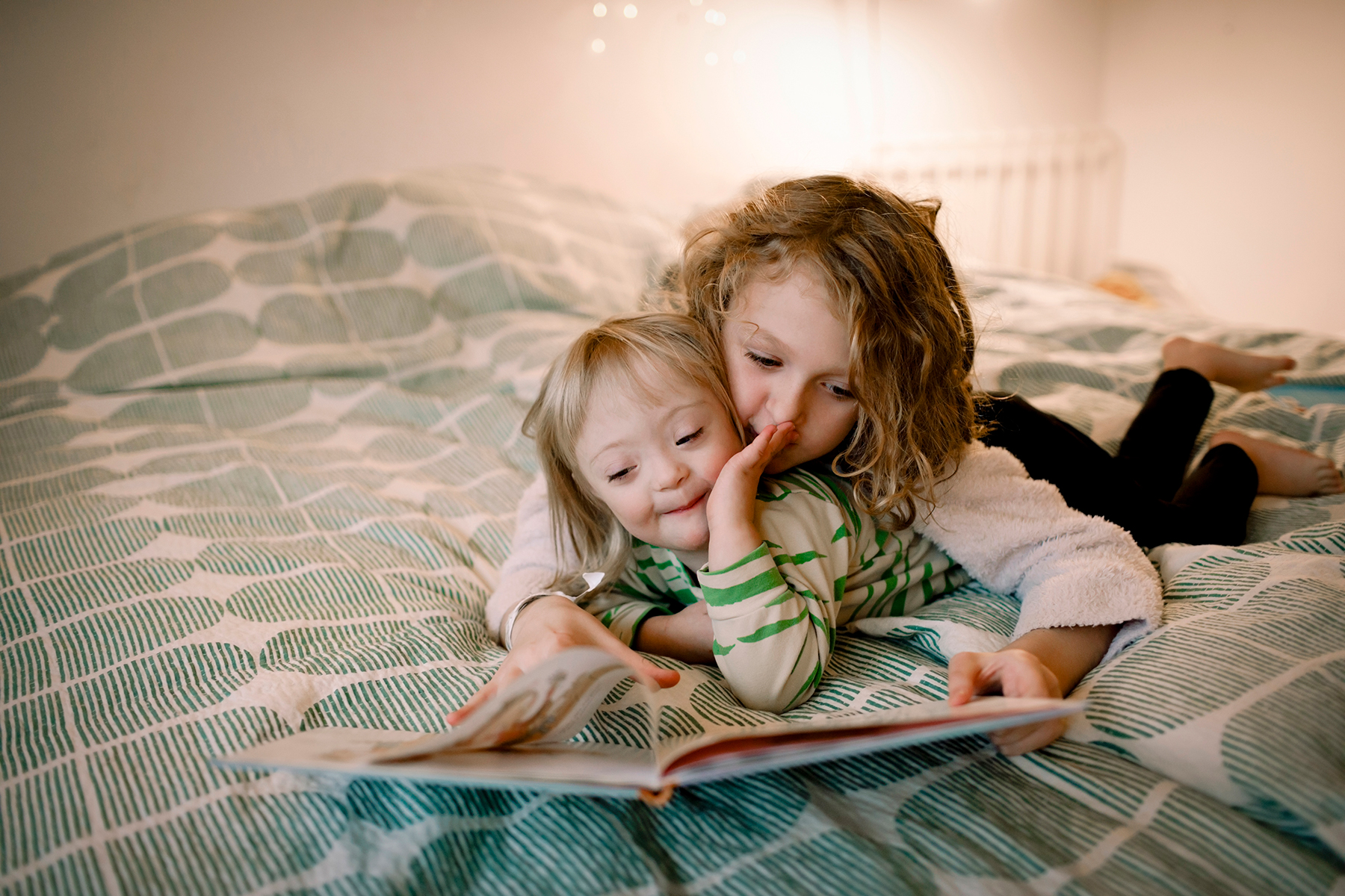 A photo of two sisters reading a book together as they lay on a bed