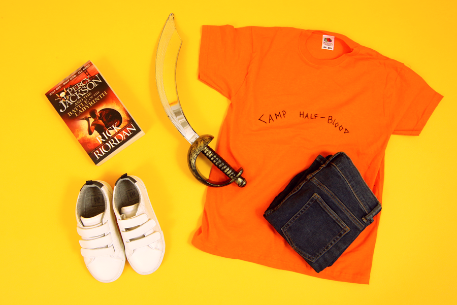A photo of a DIY Percy Jackson costume on a yellow background - costume includes a t-shirt, jeans, trainers and a fake sword