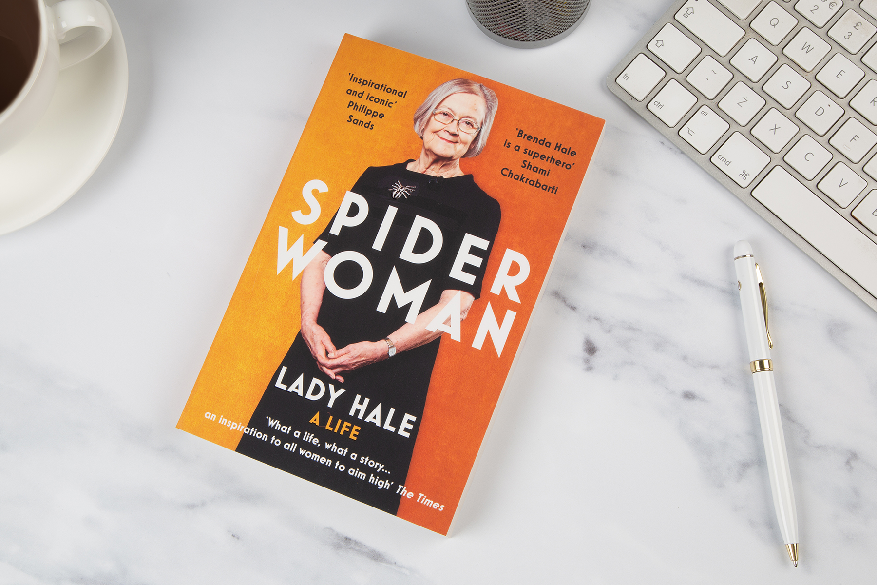 Book, Spider Woman by Lady Hale, on a marble table top, surrounded by a computer keyboard, biro pen and cup of coffee.
