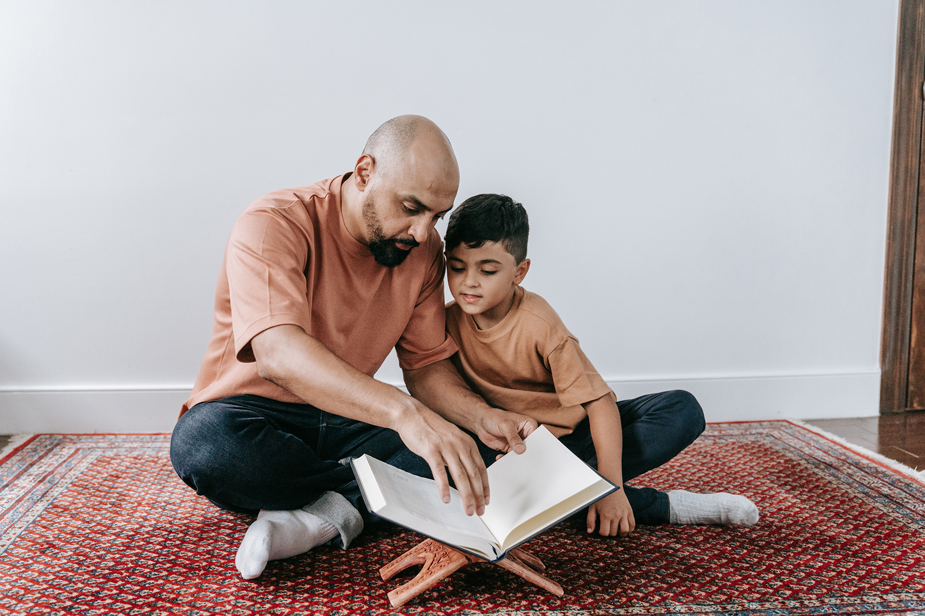 A photo of a father and son sitting on the floor as they read the Qur'an together