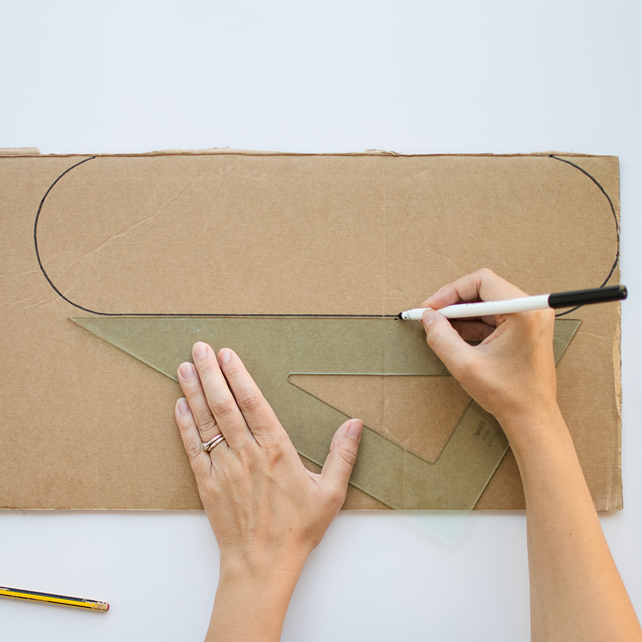 A photo of a pair of hands drawing a crocodile head shape onto a piece of cardboard