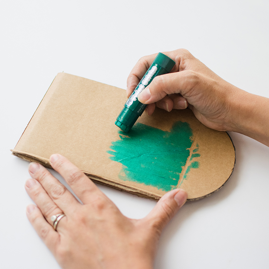 A photo of a pair of hands colouring in a crocodile-shaped piece of cardboard in green