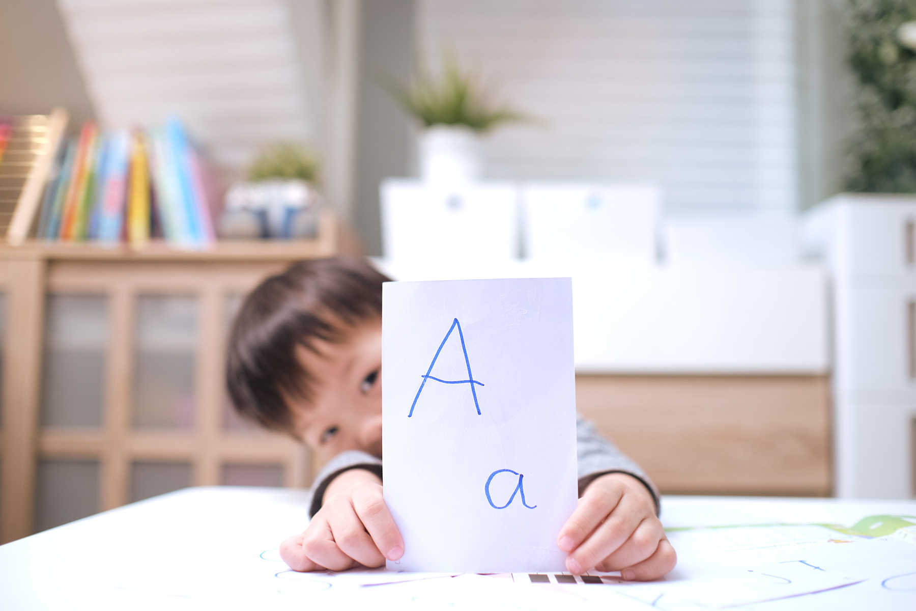 A photo of a young boy in his bedroom holding up a card that has a capital letter 'A' and a lowercase 'a' on it
