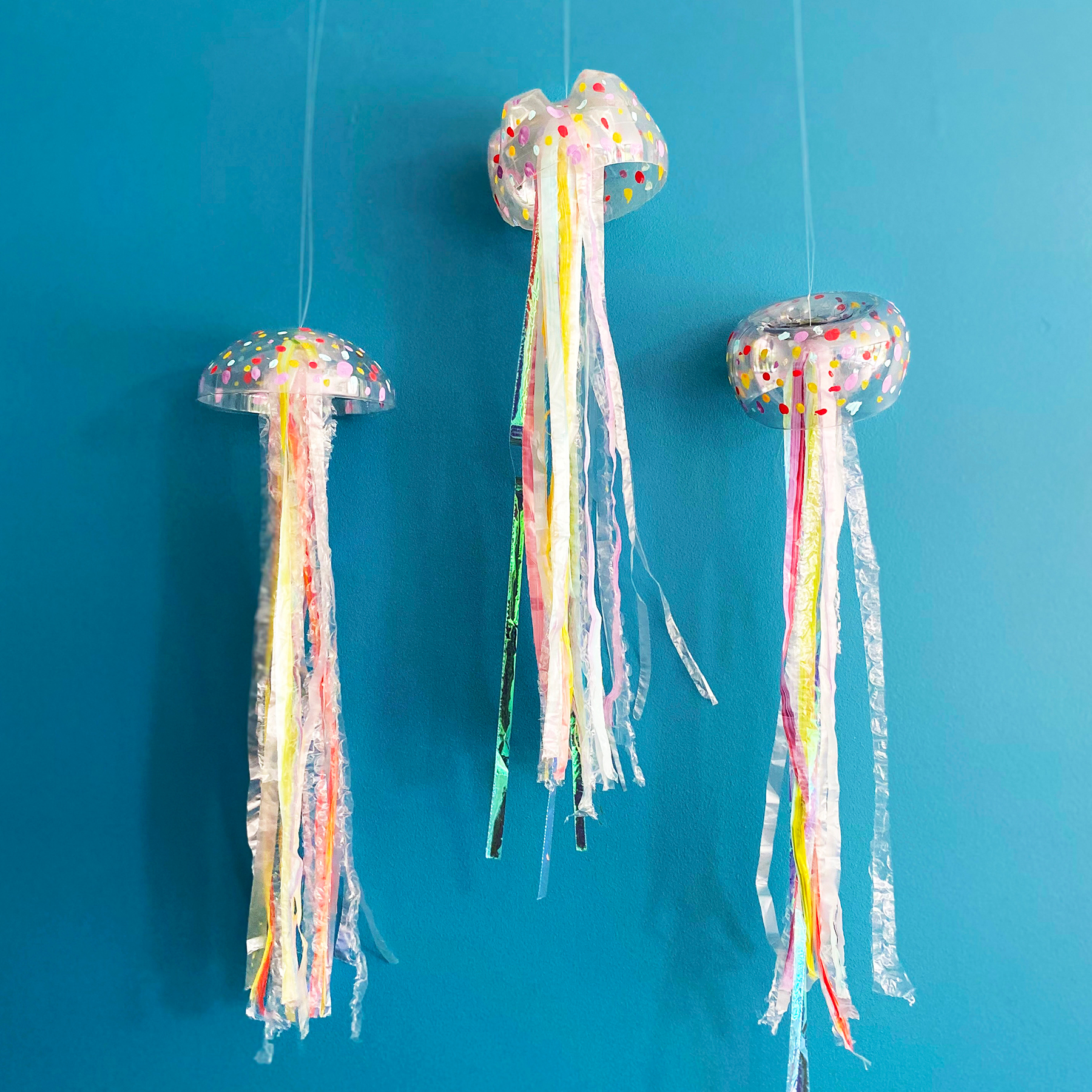 A photo of three recycled jellyfish mobiles hanging up against a blue background