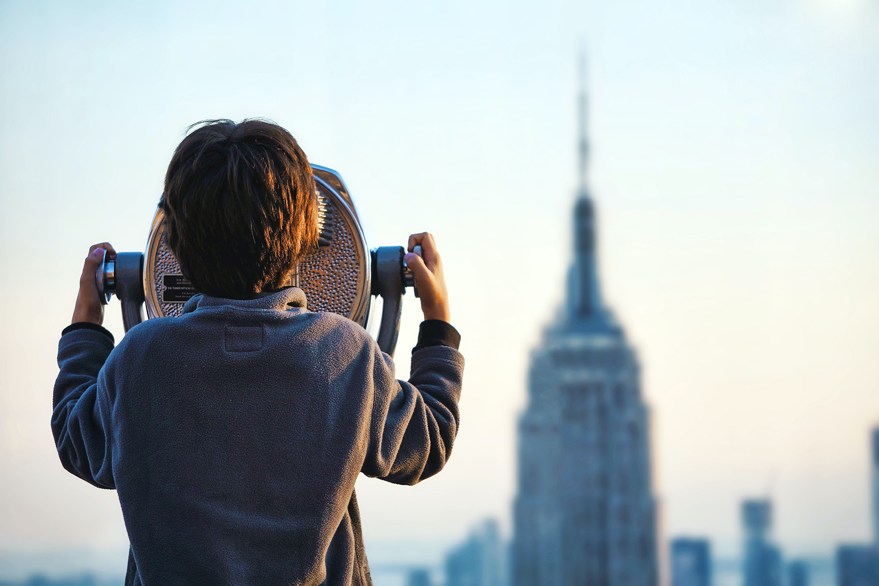 A photo of a young boy looking through a large binocular at the Empire State building in New York