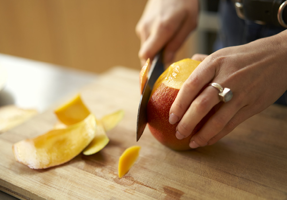 Ixta Belfrage cuts the skin off a mango.