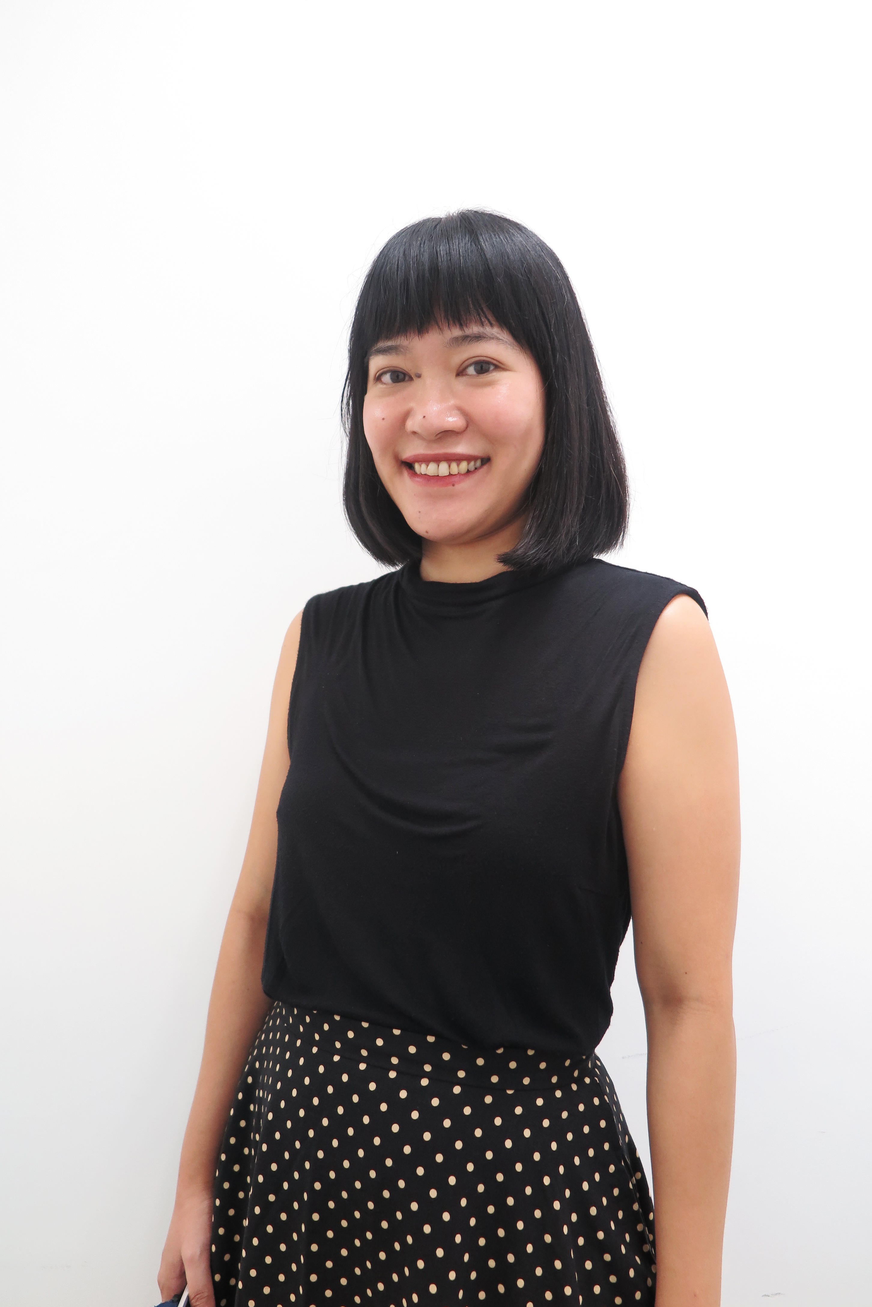 Photograph of Maesy Ang, smiling at the camera, against a white background. She is an Indonesian woman with bob-length hair, wearing a sleeveless black top and polka dot skirt.