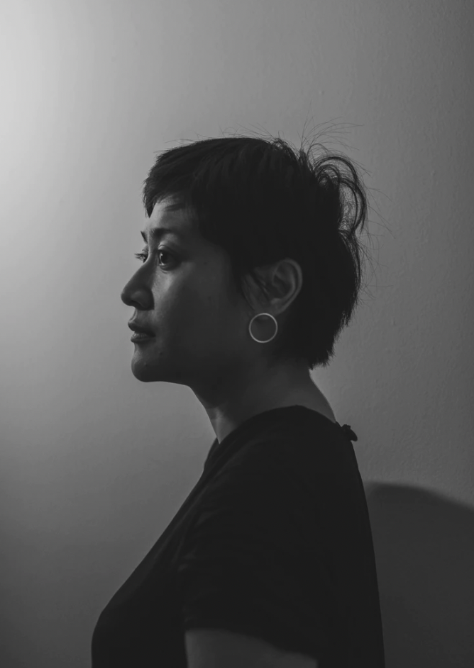 A black and white photo of Khairani Barokka in profile. She is an Indonesian woman with short hair, a visible silver earring and dark dress