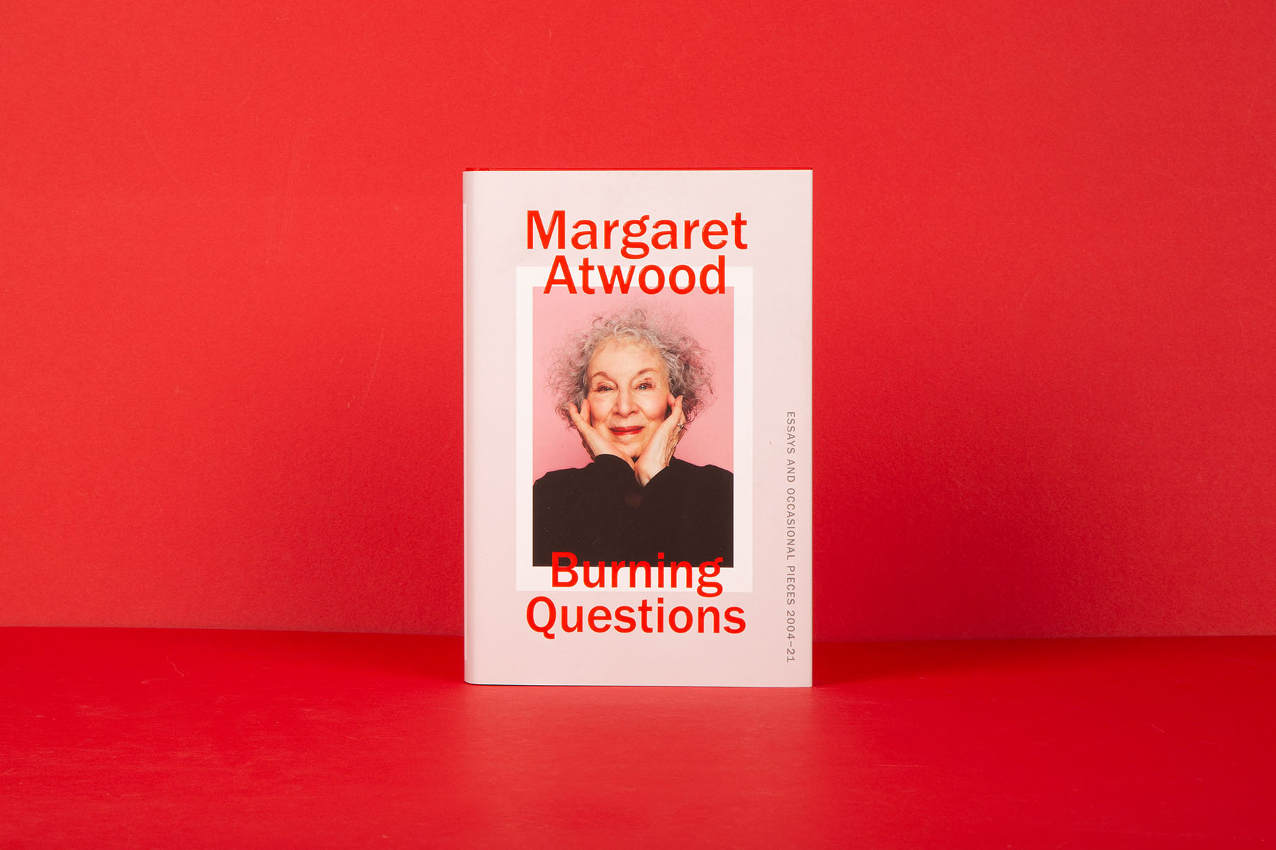 Book, Burning Questions by Margaret Atwood, standing upright against a bright red background