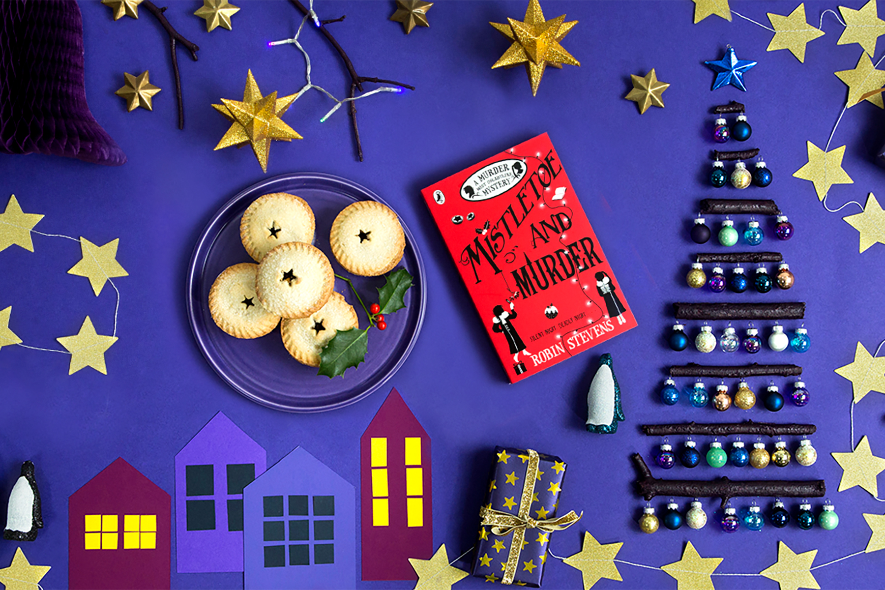 A photo of the book Mistletoe and Murder next to some mince pies on a purple background surrounded by Christmas decorations