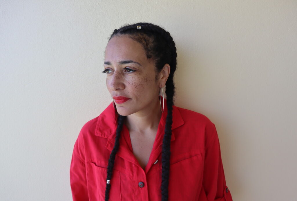 Photo Zadie Smith, Zadie stands in front of a white background wearing a red shirt.