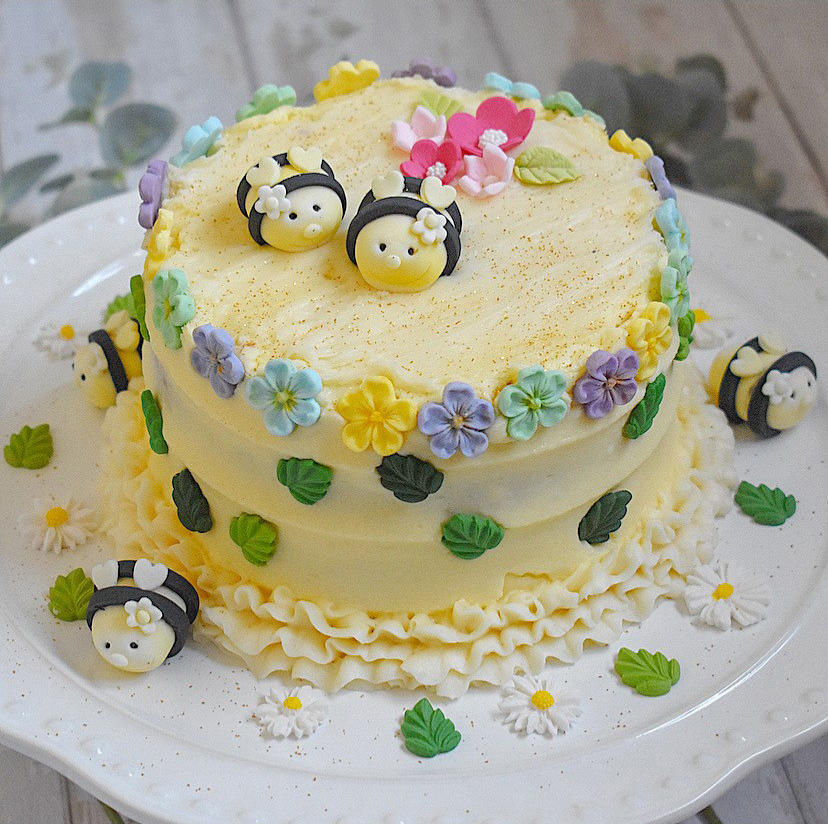 An photo of a beautiful yellow frosted cake with icing bees and flowers all over it