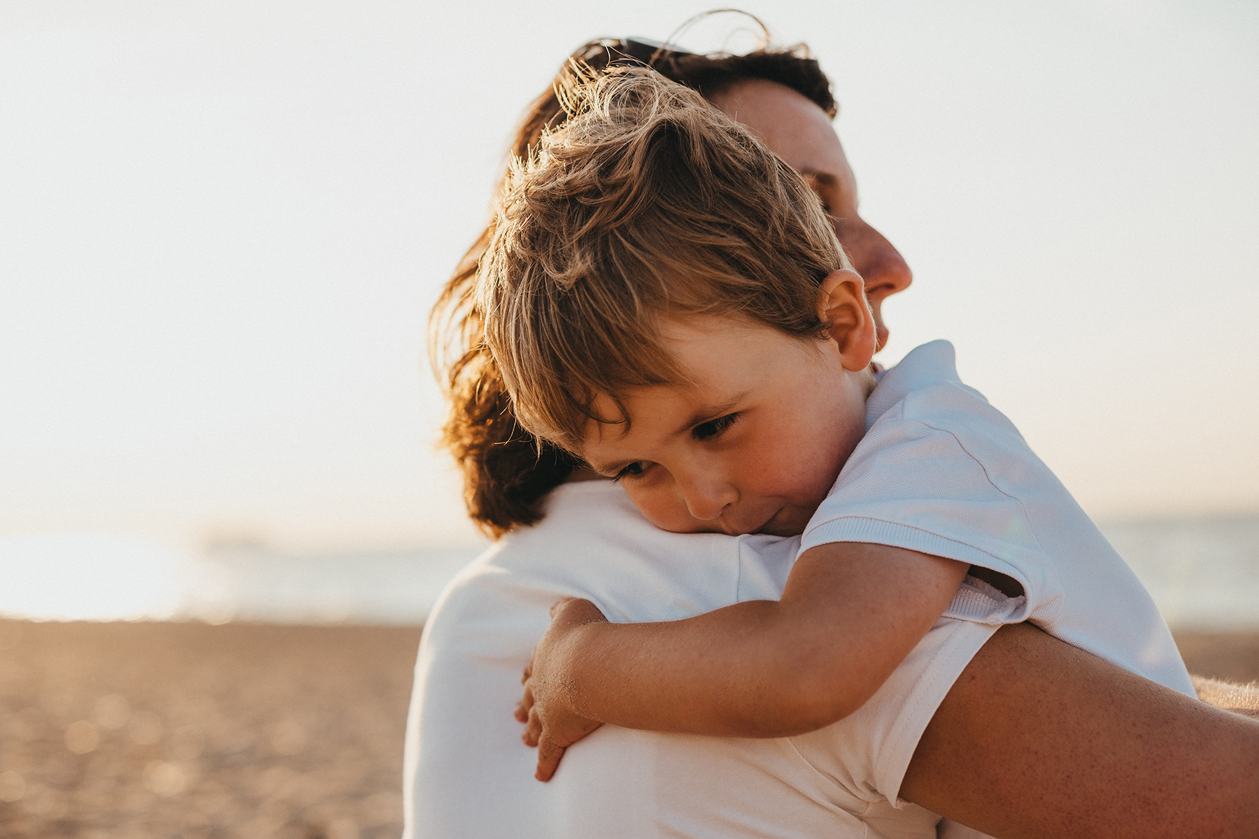 A stock photo of a woman hugging a little boy whilst they are on a beach.